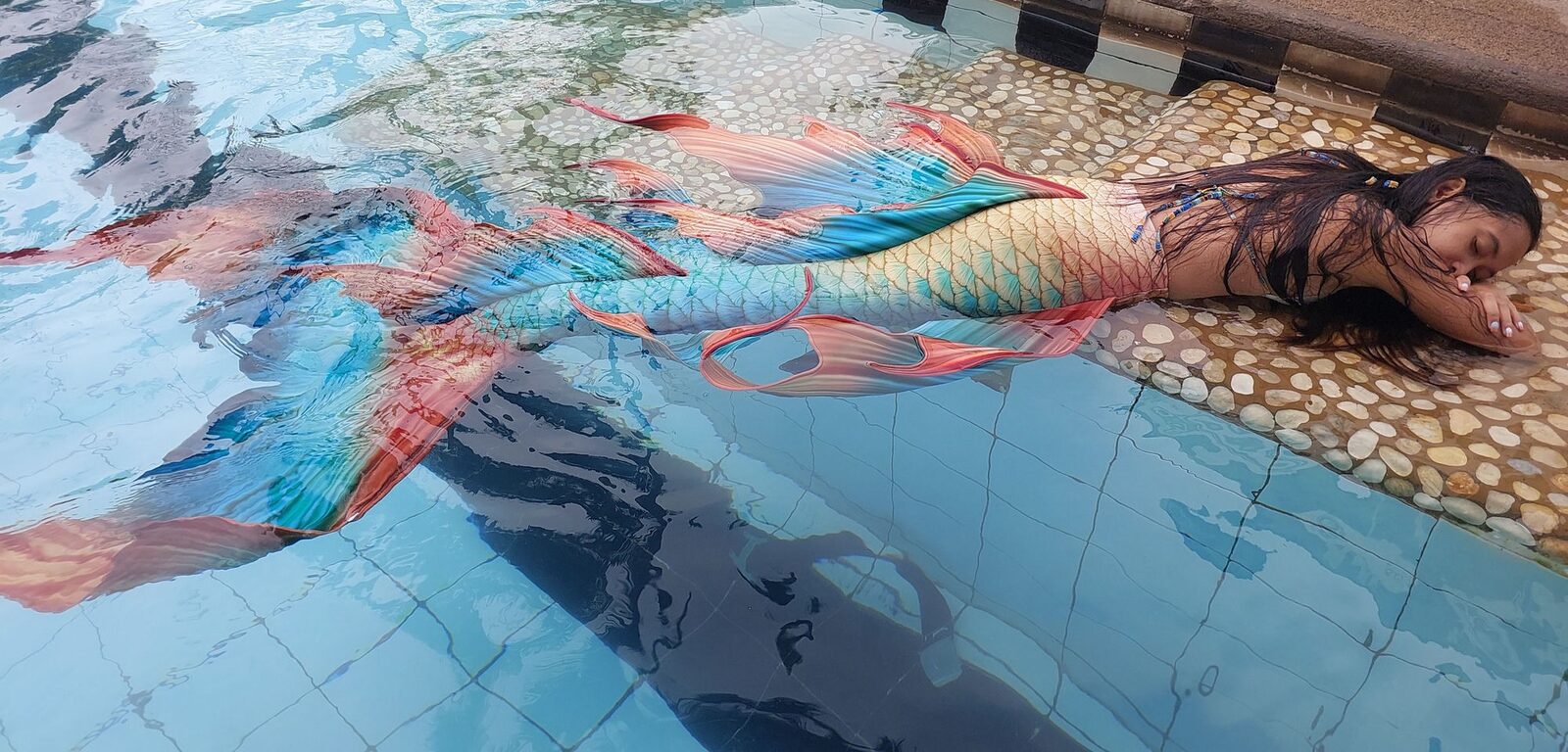 Mermaid Giona resting poolside in a colourful mermaid tail
