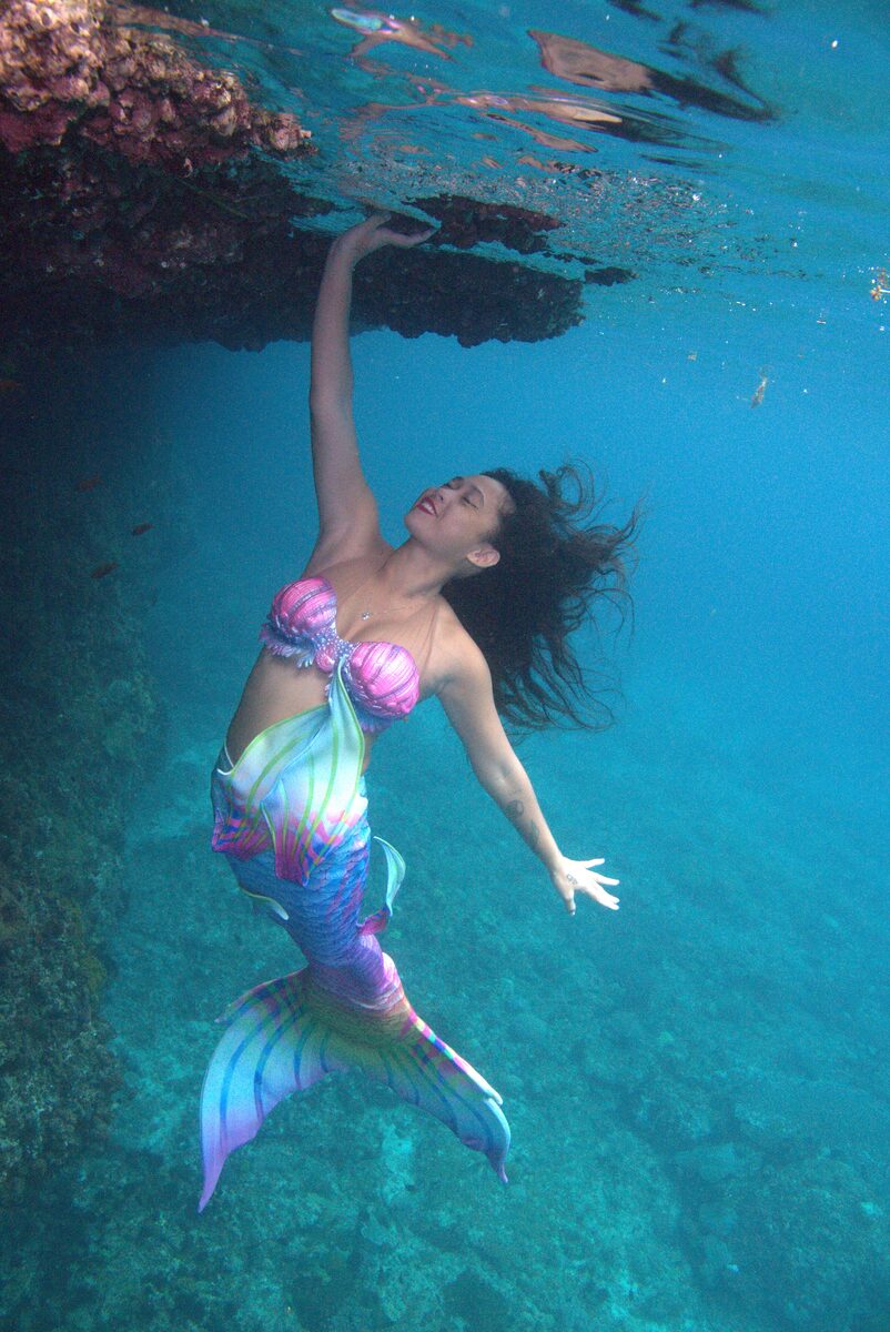 Mermaid Giona ascending beneath a rock overhang