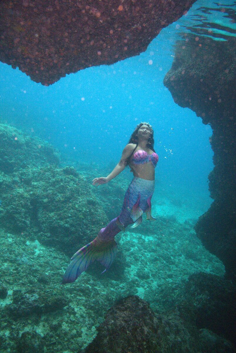 Mermaid Giona swimming beneath a rock arch